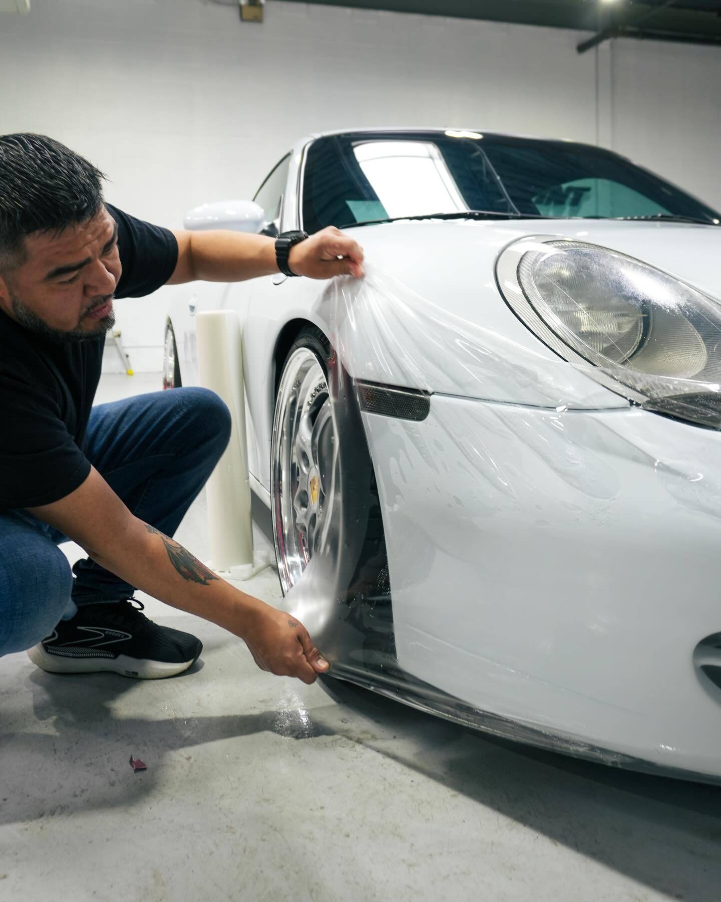 Professional technician meticulously installing XPEL Ultimate Plus Paint Protection Film PPF on Porsche front bumper