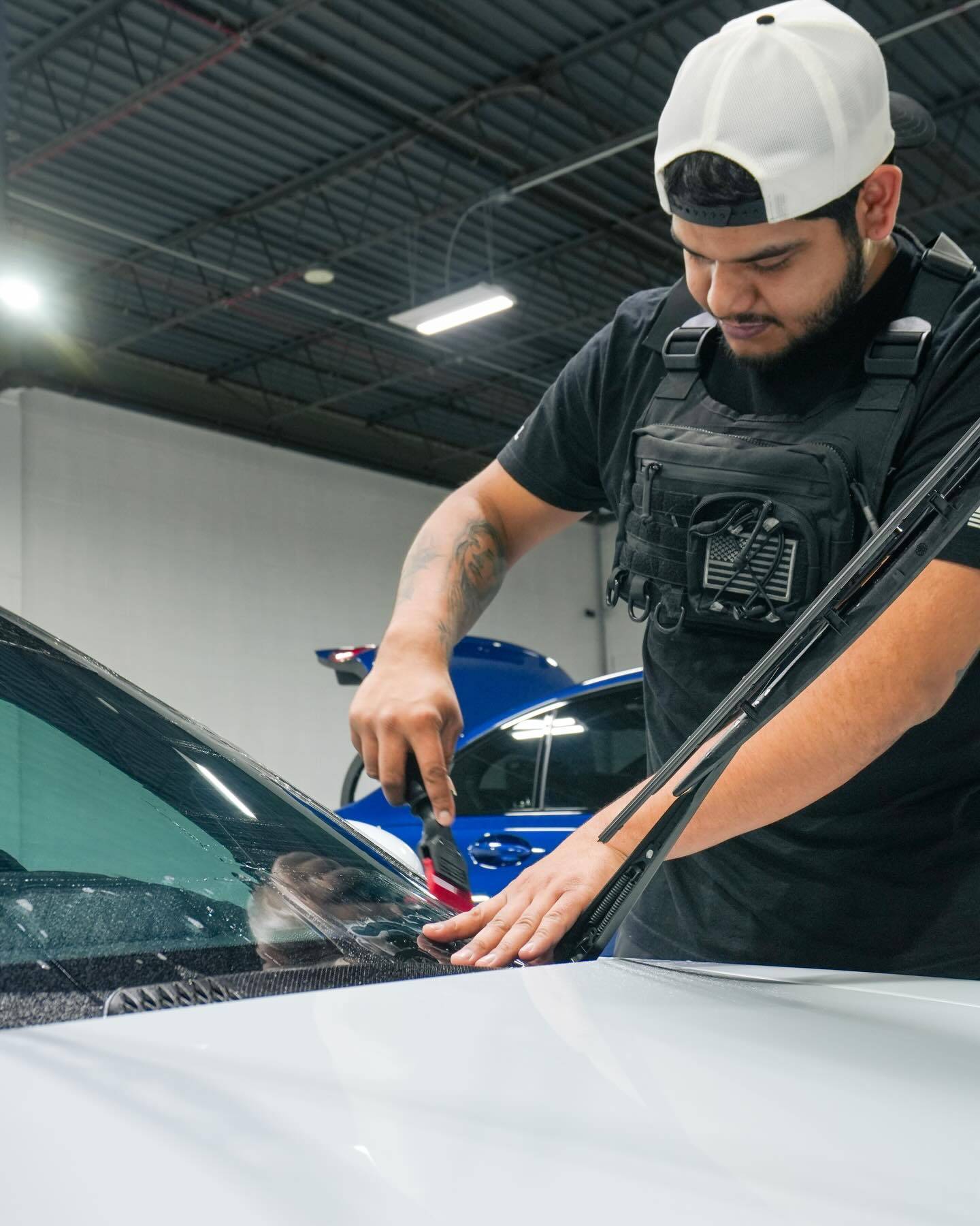 Technician installing windshield protection film squeegeeing water out on Porsche 911 glass