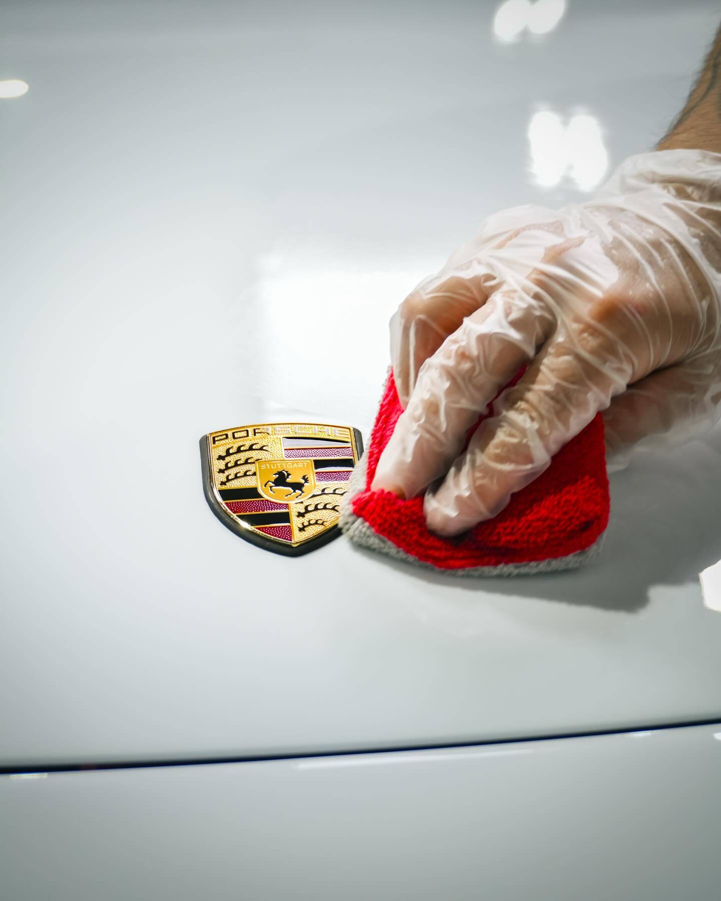 Meticulous hand wiping of Porsche front crest hood emblem using microfiber cloth