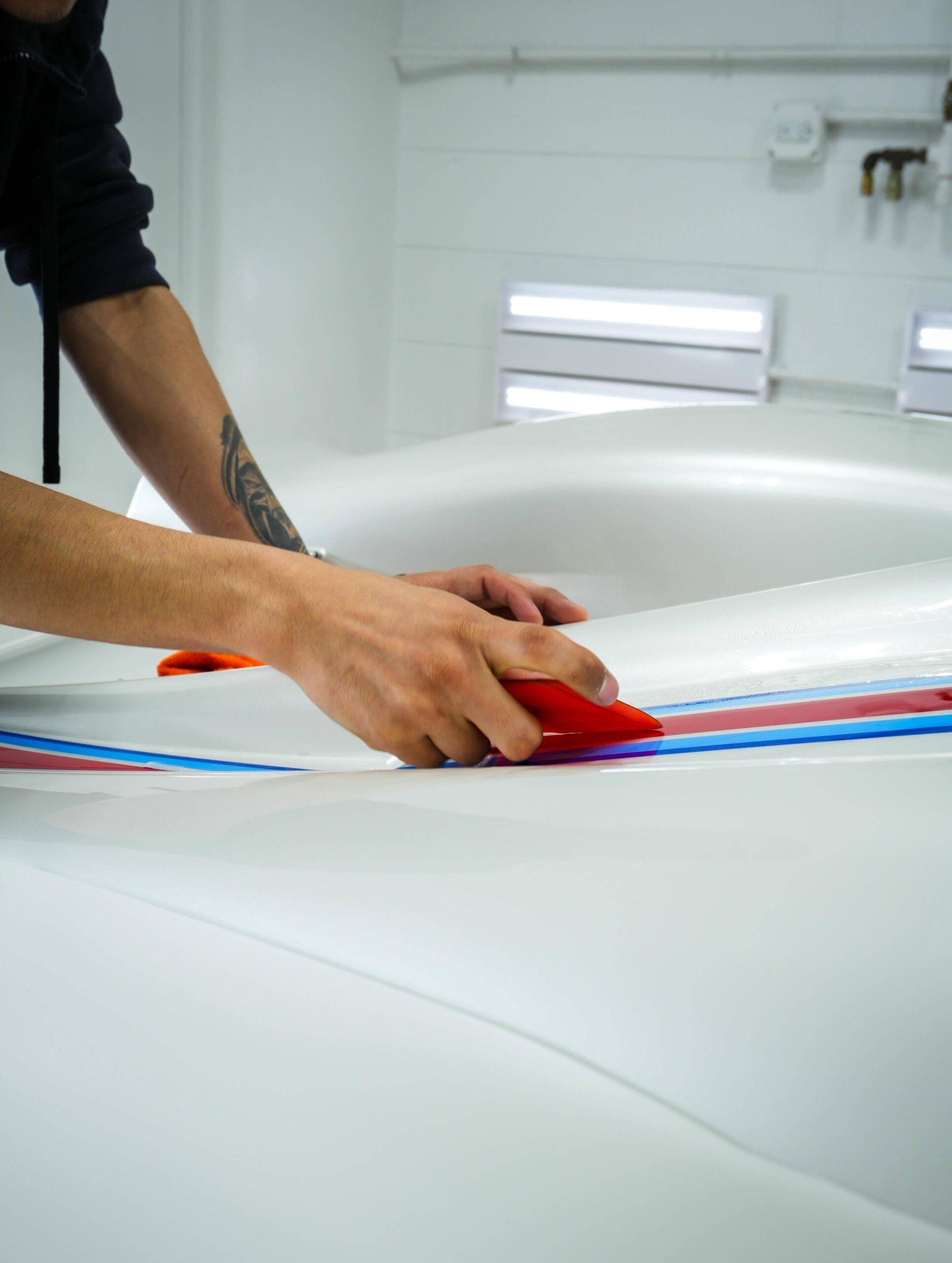 Hand squeegeeing protective film smoothly across the painted rear decklid and custom stripes